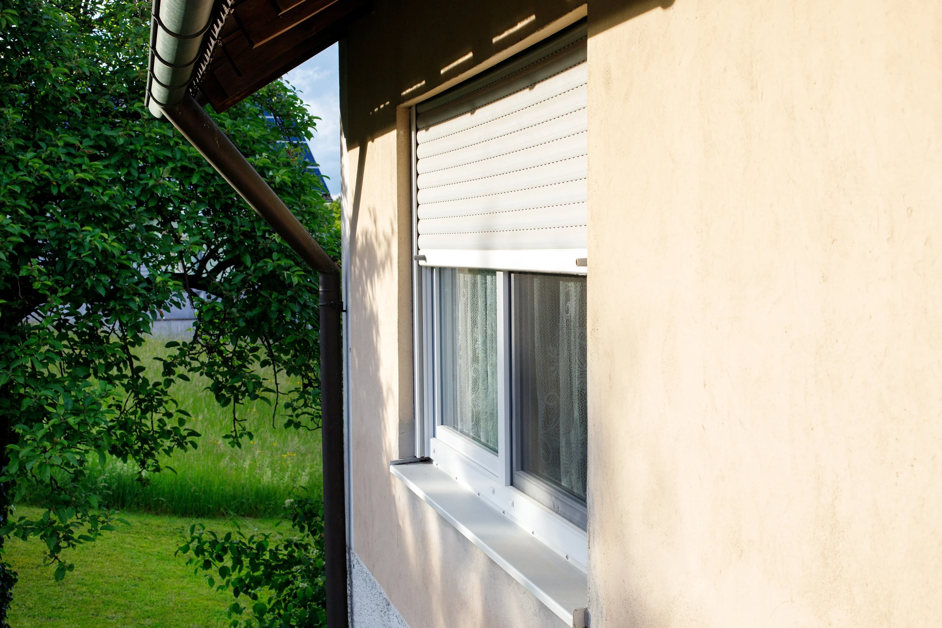 Façade extérieure de maison avec fenêtre équipée d'un volet roulant blanc en position semi-ouverte