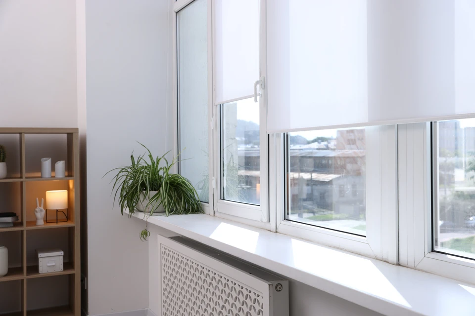 Store banne motorisé à cassette fixé en façade extérieure d'une maison contemporaine en enduit blanc, toile rayée gris et blanc dépliée, montrant l'installation professionnelle du produit sur la menuiserie.