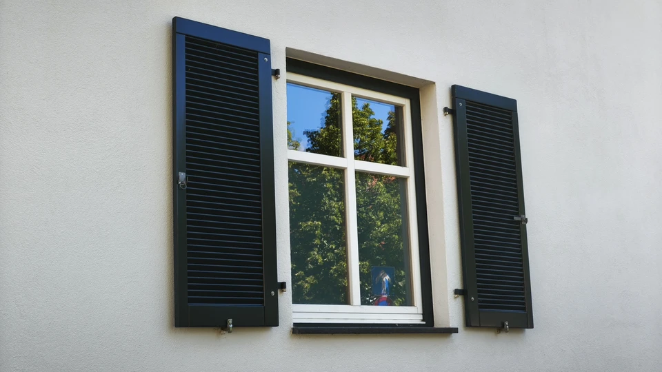 Façade extérieure d'habitation avec volets battants fermés en aluminium blanc à lames orientables