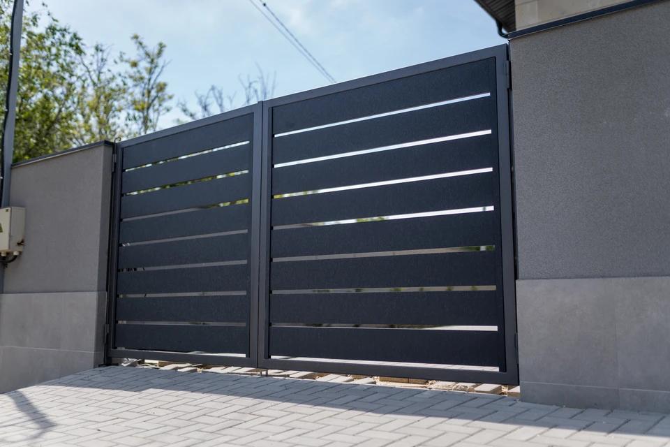 Portail double battant en aluminium laqué gris anthracite (RAL 7016), serti entre deux piliers en pierre calcaire taillée