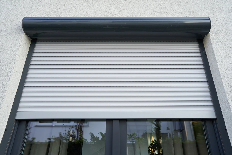 Façade extérieure d'un bâtiment avec volet roulant métallique bleu fermé, monté sur mur crépi blanc